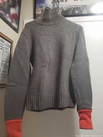 Front view of gray sweater with orange cuffs hanging