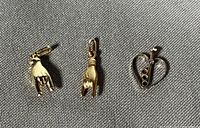 Three pendants laid out: two gold hand pendants and one heart pendant