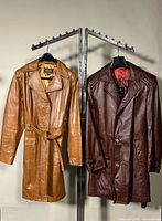 Two leather trench coats hanging, full view of both