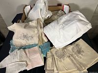 Overview of assorted embroidered and plain napkins, teal, pink, cream, white fabrics