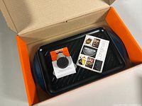 Box opened showing grill plate, cleaning brush in packaging, and manual