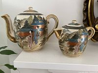 Front view of teapot and creamer showing hand-painted scenes and gilt handles