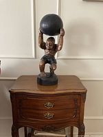 Front view of carved Atlas figure holding black sphere on black base