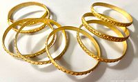 Eight gold-tone textured bangles arranged overlapping on white background