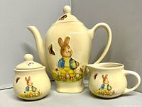 Front view of pitcher, creamer and sugar bowl showing Peter Rabbit decoration