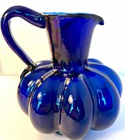 Front view of cobalt blue melon-shaped glass pitcher with handle and flared spout