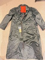 Front view of full-length black raincoat showing zipper, snaps, and red lining