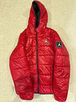 Front view showing red puffer jacket, hood, chest Jumpman logo, sleeve patch