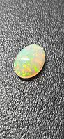 Oval cabochon opal showing multicolor play-of-color on black background
