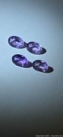 Four faceted oval purple amethysts on neutral background