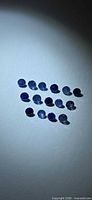 Fifteen blue sapphires arranged on white background under spotlight