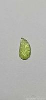 Leaf-shaped carved green tourmaline gemstone on neutral background