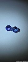 Two round violet-blue tanzanite gemstones on neutral background
