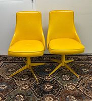 Front view of both yellow vinyl swivel chairs on patterned rug