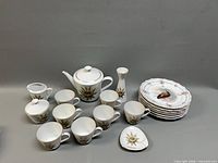 Full lot layout with teapot, cups, creamer, sugar, vase, triangular plate and stack of fish plates
