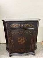 Front view of black lacquered cabinet with gold stenciling, showing drawer and door