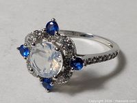 oblique view showing center clear stone, blue accent stones, pavé band