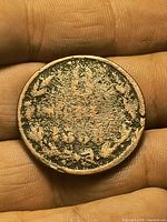 Obverse of copper coin in hand, showing shield with three lions and wreath, heavy wear