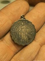 Front view of silver Miraculous Medal in hand showing inscription and figure