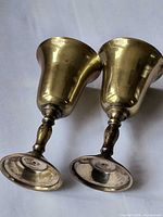 Both brass shot glasses lying side by side showing exterior finish