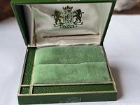 Open ring box showing interior crest, satin lining, velvet pad