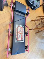 Full view of red-framed creeper with logo, headrest, casters, flashlight