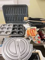 All items grouped together on countertop: splatter screen, roasting pan & broiler top, two muffin tins, brushes, tongs, oven mitts