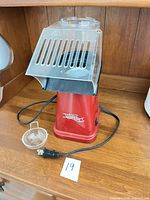 Front view of red Betty Crocker hot air popper with clear chute, cup and cord