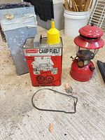 Lantern, fuel can with spout, case, wire handle on floor