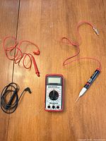 Multimeter, red lead with probe, black lead, continuity tester displayed on wood surface