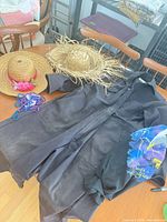 Entire lot laid on table: black coat, two straw hats, bead strand