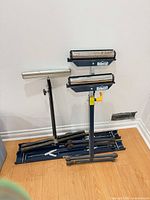 Collapsed blue Mastercraft sawhorses stacked on floor beside two roller stands