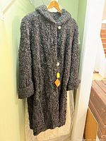 Full view of black curly fur coat on hanger