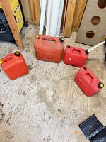 Group shot of four red plastic fuel cans in varying sizes on floor