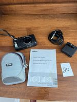 Camera, battery charger, USB cable, manual and carry pouch arranged on wooden surface