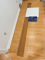 Long brown pegboard strip, white square panel and blue bin with hooks on floor