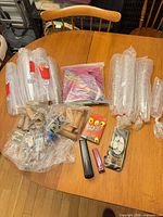 Overview of lot: plastic cup sleeves, bag of straws, coin wrappers, staplers, Face Off game, ping-pong balls