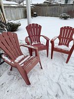 Three red plastic Adirondack chairs on snow-covered patio
