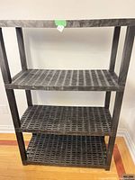 Front view of black plastic four-tier shelving unit against wall