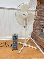 Pedestal fan and mini tower fan side by side on hardwood floor against wall