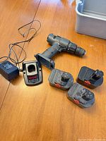 Drill, charger, three batteries on tabletop