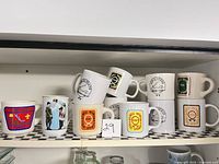 Shelf holding eleven white ceramic mugs decorated with various scouting badges and graphics