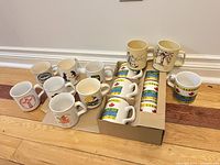 Full group of 15 scouting mugs arranged on floor showing front designs