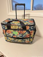 Front view of floral rolling sewing machine bag showing front zip pocket and top handles