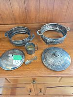 All items arranged on wooden surface: two footed dishes, two lids, cup, spoon