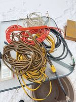 Pile of assorted extension cords and cables on glass table in snow with yellow metal box visible