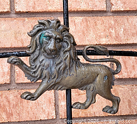 Full view of cast metal lion ornament on black frame against brick