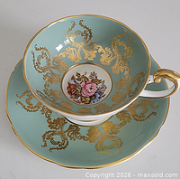 Cup on saucer showing overall teal ground with gold scrollwork and floral medallion