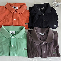 Four folded Lacoste polo shirts in orange, black, mint green and brown