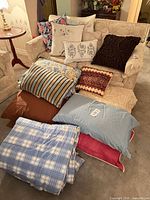 Group of throw pillows, bed pillows and blankets displayed on sofa and floor